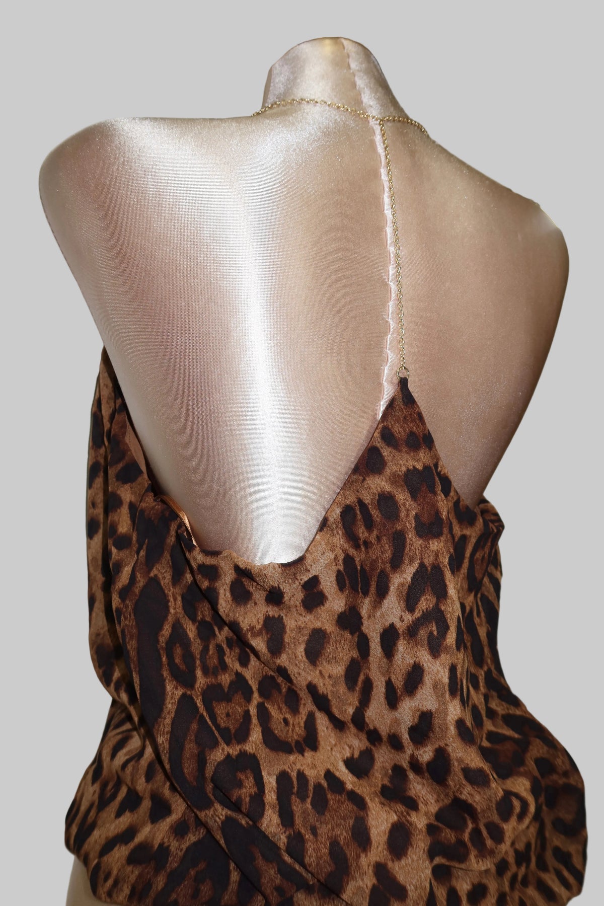A leopard print camisole top, featuring thin spaghetti straps and a draped open-back design.